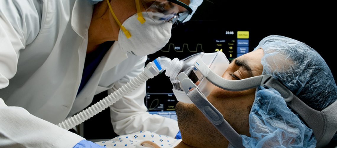 Female caucasian doctor checking on Covid-19 infected patient while connected to a ventilator at a hospital room